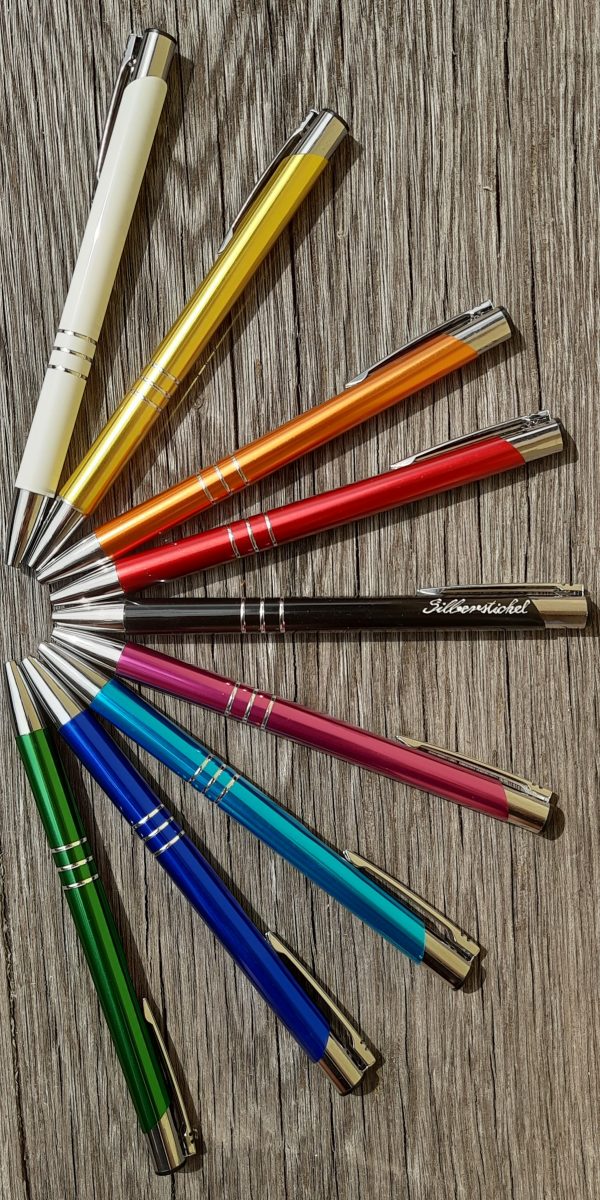 Kugelschreiber in verschiedenen Farben liegen in einem Halbkreis angeordnet. Der mittlere Kugelschreiber ist versehen mit einer Handgravur. Die Gravur zeigt in feiner Schreibschrift das Wort Silberstichel.